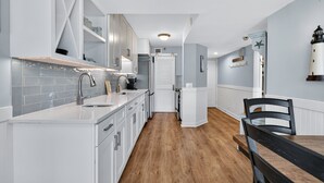 A modern kitchen with white cabinetry, a wooden floor, a dining area with a black table and chairs, and a view of the sea through a window. - Updated Direct Oceanfront Condominium with Great Amenities (St. Simons Island)