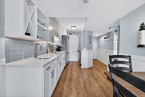 A modern kitchen with white cabinetry, a wooden floor, a dining area with a black table and chairs, and a view of the sea through a window. - Updated Direct Oceanfront Condominium with Great Amenities (St. Simons Island)