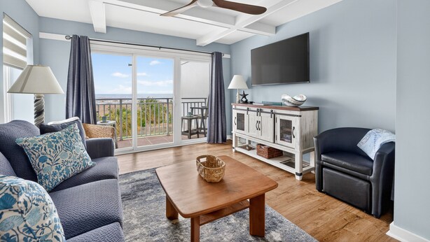 A living room with a sofa, a coffee table, a TV, and a balcony with a view. - Updated Direct Oceanfront Condominium with Great Amenities (St. Simons Island)