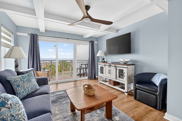 A living room with a sofa, a coffee table, a TV, and a balcony with a view. - Updated Direct Oceanfront Condominium with Great Amenities (St. Simons Island)