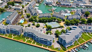 Eine Luftaufnahme eines Yachthafens mit Booten, einem Tennisplatz und Wohnhäusern.