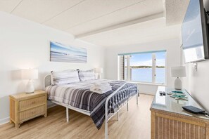 Ein Schlafzimmer mit Bett, Nachttischen, einem Fenster mit Blick und einem an der Wand montierten Fernseher.