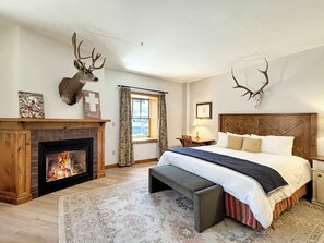 Ein Schlafzimmer mit Kamin, einem Bett mit Holzvorhang und einer Bank, sowie Hirschgeweihen an der Wand.