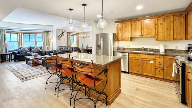 A spacious living area with a dining table, kitchen with wooden cabinets, and a large window. - NEW LISTING | Beautiful Lodge at Mountaineer Square 2 Bedroom (Crested Butte)