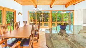 Uma área de refeições com mesa e cadeiras de madeira, janelas amplas e um candelabro.