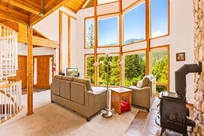 A spacious living room with a large window, a fireplace, and a cozy sofa. - Mountain View Home | Near Leavenworth | Sleeps 8 (Leavenworth)