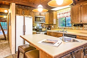 A kitchen with wooden cabinets, a refrigerator, a microwave, and a large island with a magazine.