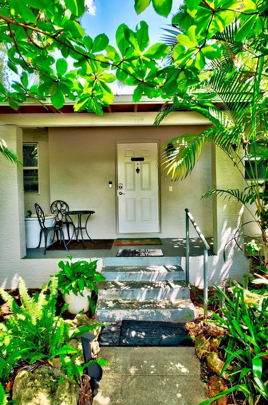 A house with a white door, a porch with a table and chairs, and steps leading to the entrance.