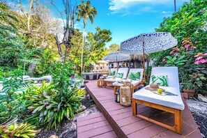A tropical garden with wooden deck seating, a thatched-roof structure, and lush greenery. - Heated Pool/Hot Tub/10 min Beach & Airport (Fort Lauderdale)