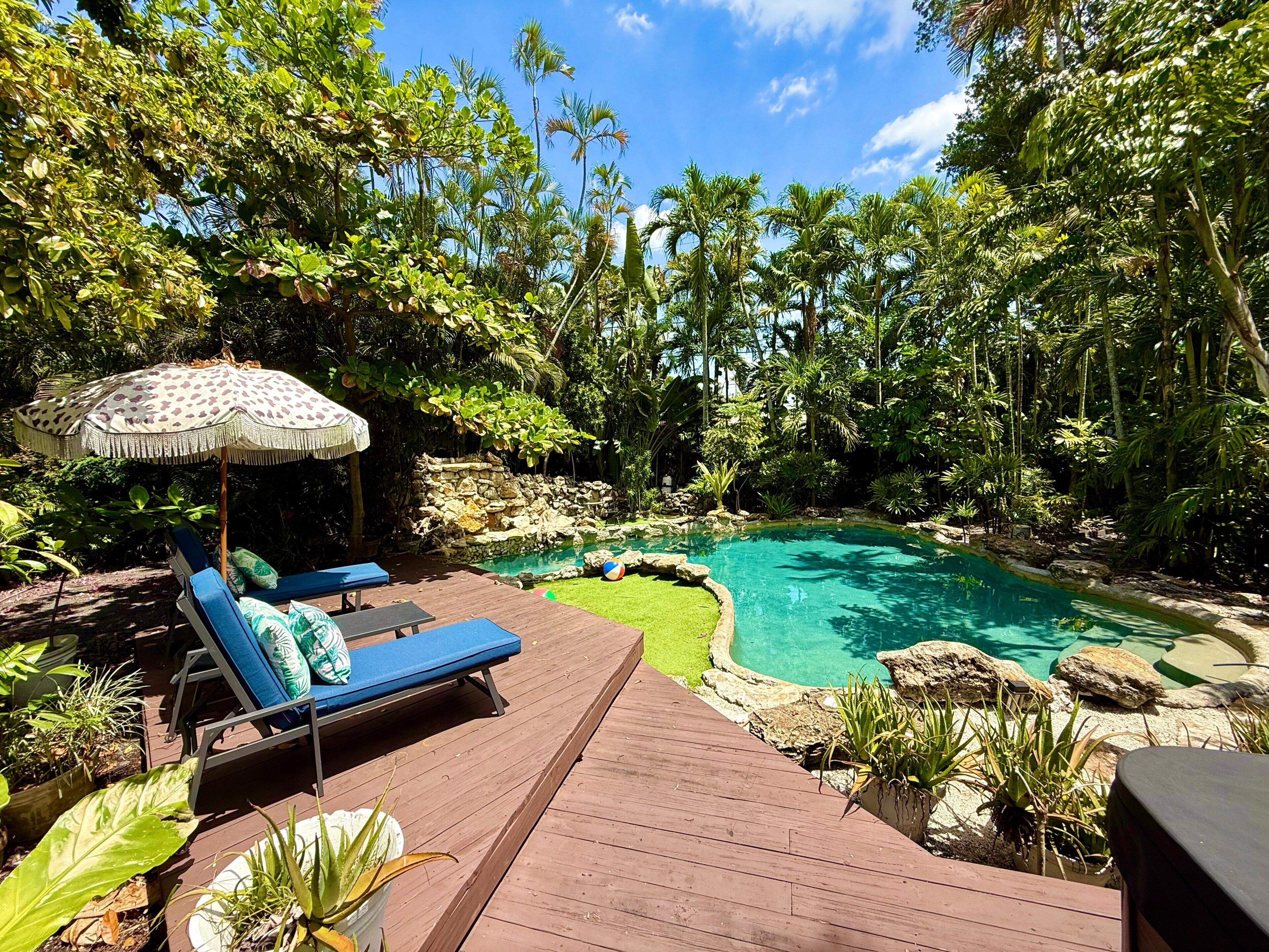 A wooden deck with lounge chairs and an umbrella, a small pool surrounded by tropical vegetation.