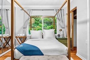 A bedroom with a canopy bed, a bedside table with a lamp, and a view of greenery outside. - Heated Pool/Hot Tub/10 min Beach & Airport (Fort Lauderdale)