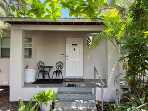 A house with a white exterior, a front door, two chairs, a small table, and a potted plant. - Heated Pool/Hot Tub/10 min Beach & Airport (Fort Lauderdale)