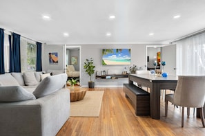 A modern living room with a grey sofa, wooden coffee table, and a dining area with a dark wooden table and chairs. - Heated Pool/Hot Tub/10 min Beach & Airport (Fort Lauderdale)