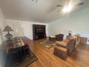 A living room with a wooden floor, a television on a stand, a sofa, a coffee table, and a lamp.