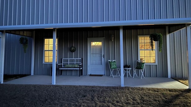 Een gebouw met een overdekte veranda, een deur en twee ramen met hangplanten.