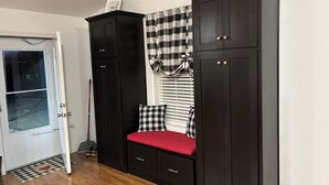 Een kamer met een zwarte garderobe, een bankje met een rode kussen, een zwart-wit vloermat en een deur met een ruitpaneel.