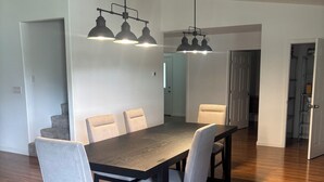 Een eetgedeelte met een houten tafel en stoelen, hanglampen, en een gang naar andere kamers.