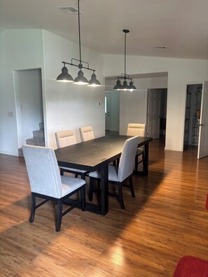 A dining area with a wooden table and chairs, pendant lighting, and a hallway leading to other rooms.