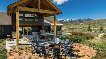 A two-story wooden house with a patio area featuring outdoor furniture and a hot tub.