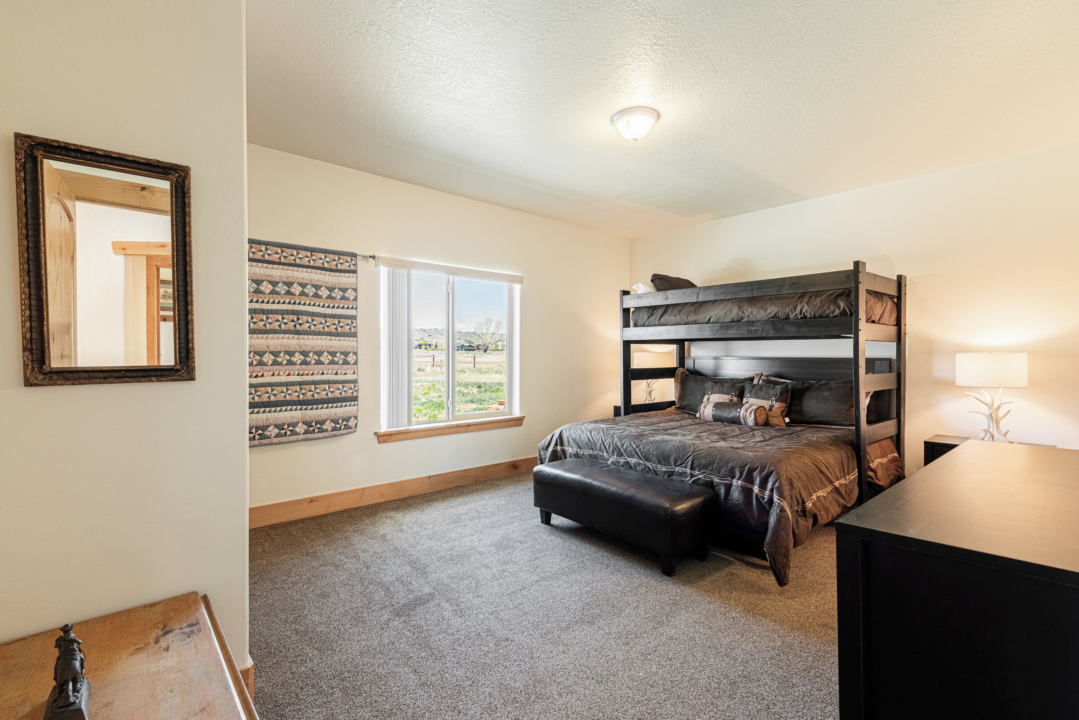 A bedroom with a bunk bed, a window with a view, a desk, and a mirror.