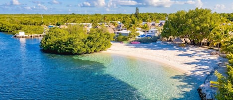 Eine Küstenlandschaft mit klarem Wasser, einem Sandstrand und einer kleinen Insel mit Gebäuden.