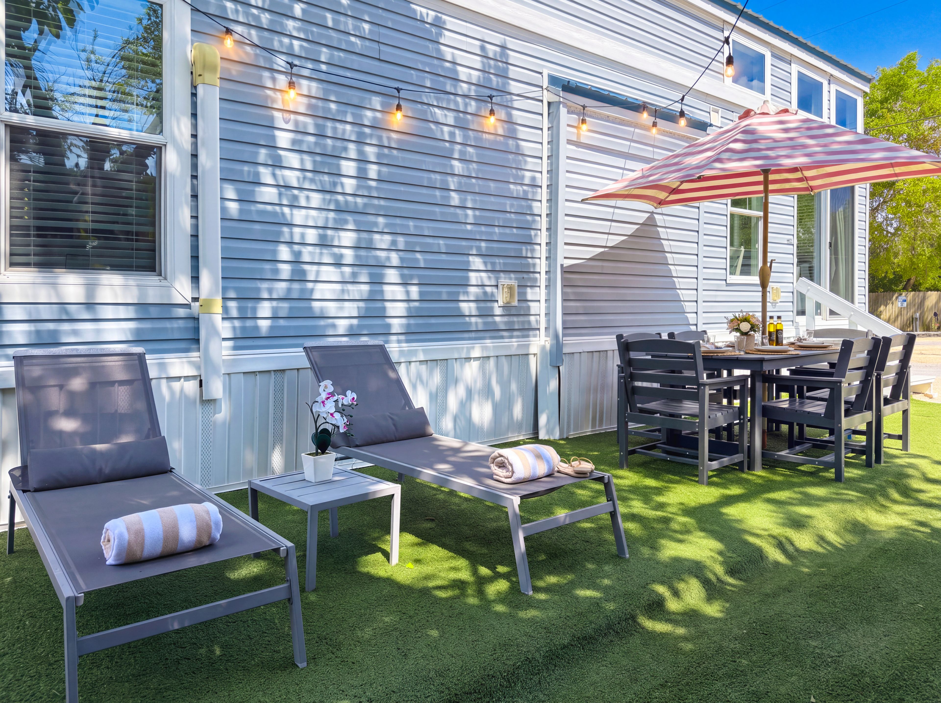 Une terrasse avec des meubles d’extérieur, notamment des chaises et une table, ainsi qu’un parasol à rayures.