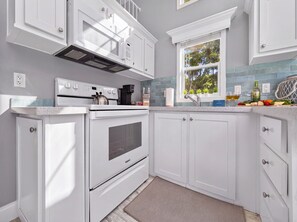 A kitchen with white cabinetry, a stainless steel range hood, a built-in oven, and a window with a view of trees.