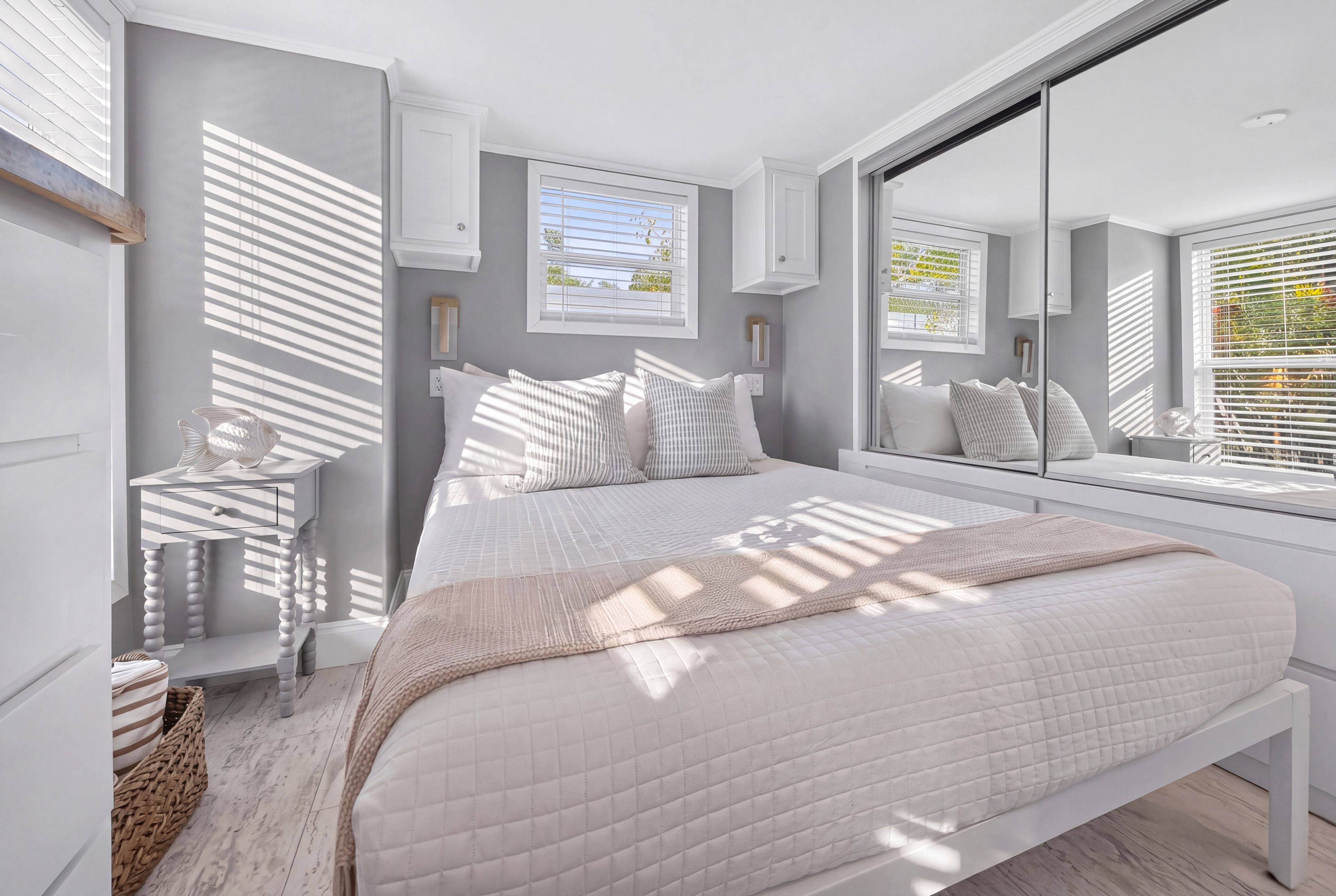 A bedroom with a large bed, a bedside table, a mirror, and a window with blinds.