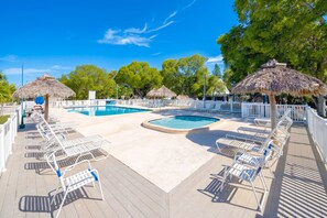 Un área de piscina con varias piscinas, sillas de descanso y sombrillas de paja.