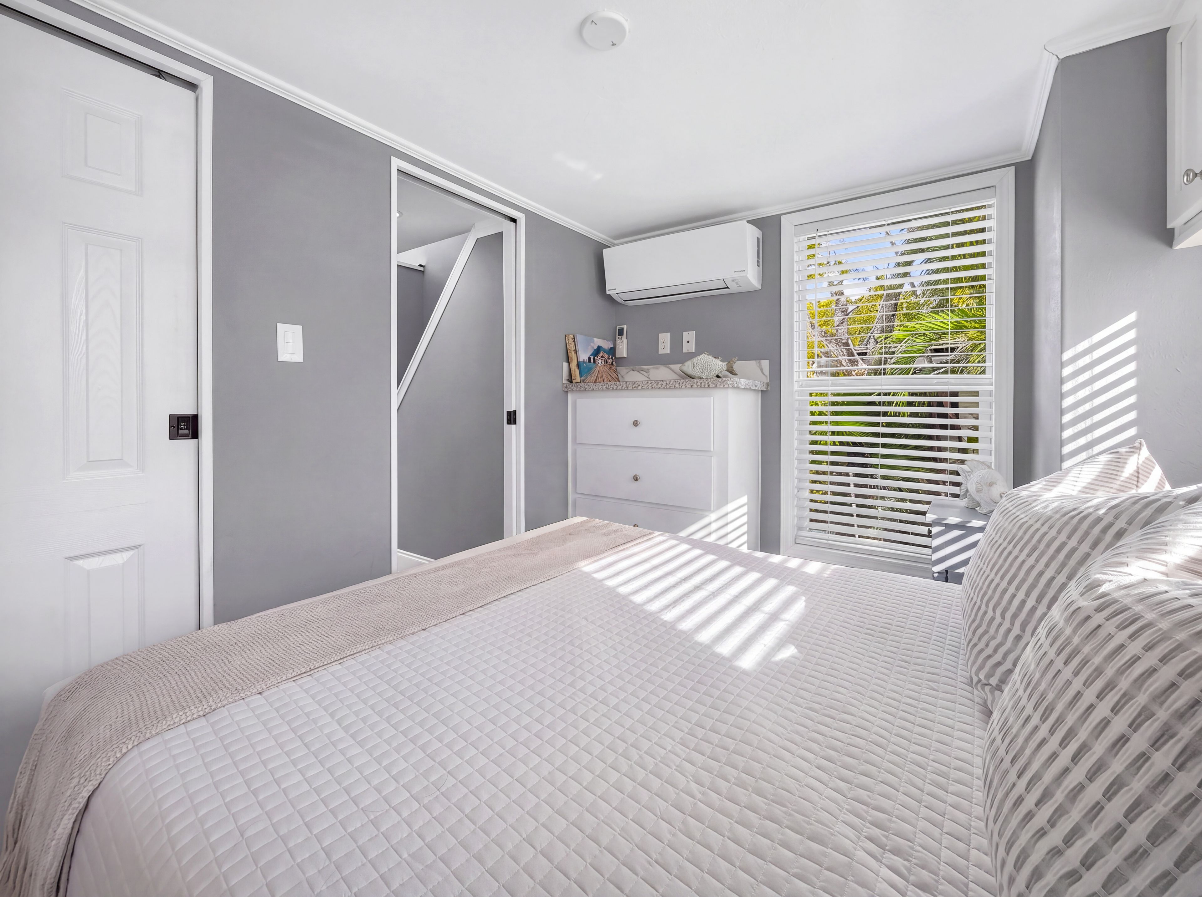 Quarto com cama, penteadeira, janela com persianas e ar condicionado.