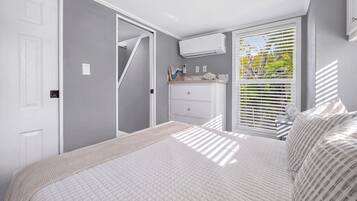 Quarto com cama, penteadeira, janela com persianas e ar condicionado.