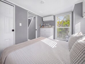 A bedroom with a bed, a dresser, a window with blinds, and an air conditioning unit. - New Tiny Home-Paddle Boards, Kayaks, Pool, Marina (Key Largo)