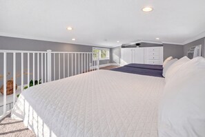 A bedroom with a large bed, a white railing, a window, and a built-in wardrobe.