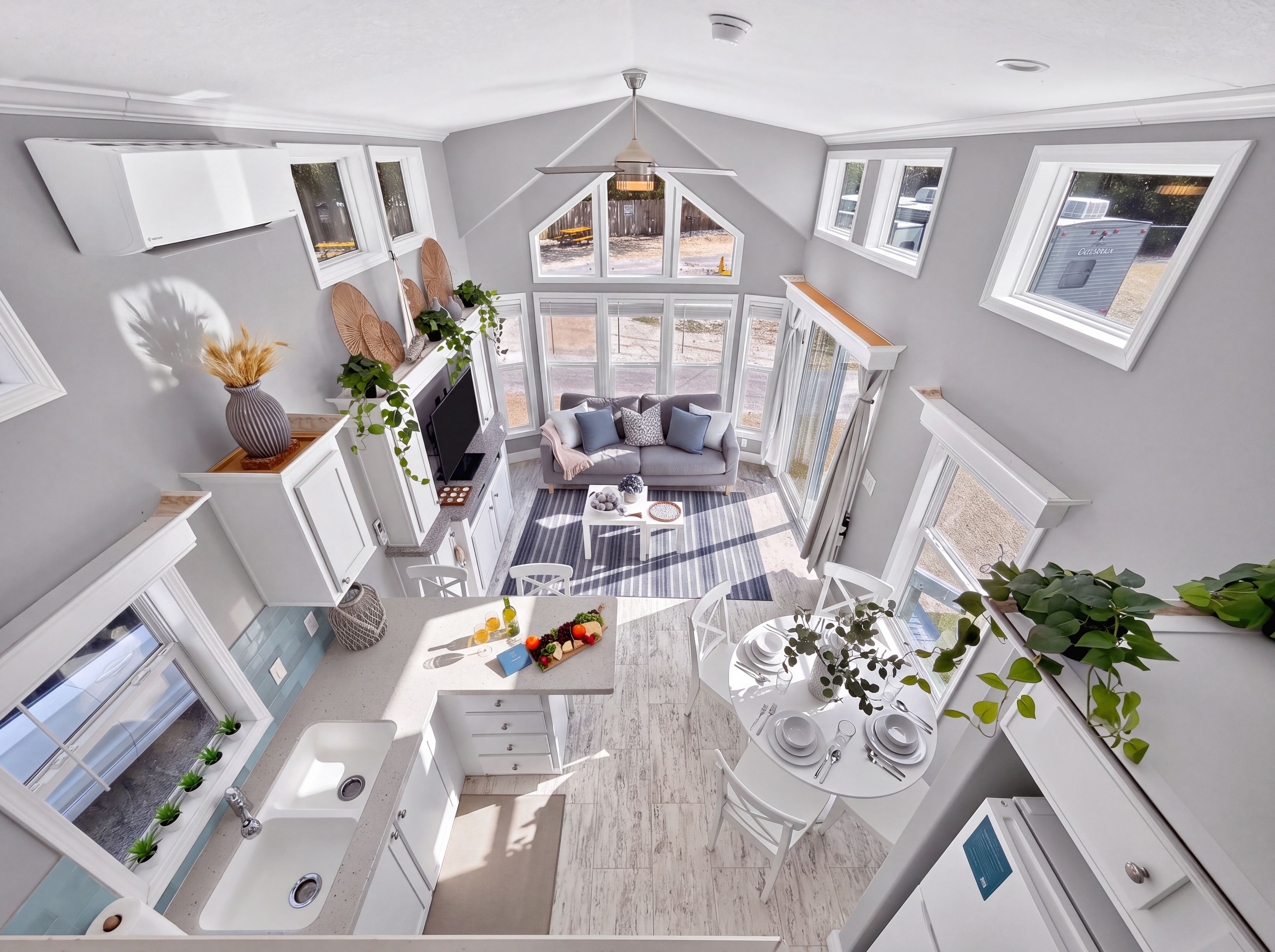 Un intérieur moderne comprenant une cuisine, un coin repas et un espace de vie, avec une grande fenêtre, un ventilateur de plafond et des appareils électroménagers intégrés.