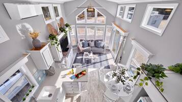 Un intérieur moderne comprenant une cuisine, un coin repas et un espace de vie, avec une grande fenêtre, un ventilateur de plafond et des appareils électroménagers intégrés.