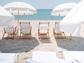 Des chaises de plage et des parasols sur une plage de sable, avec l’océan en arrière-plan.
