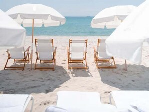 Ein Strand mit weißen Sonnenschirmen und Holzliegen, die zum Meer ausgerichtet sind.