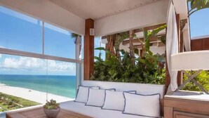 Un terrazzo in legno con divano e tavolo, una pianta in vaso e vista sulla spiaggia.