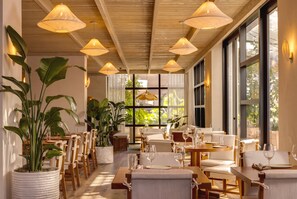 A dining area with multiple tables and chairs, large windows, and hanging pendant lights. - 1 Hotel South Beach | 2BR, 14th FL Balcony, water view (Miami Beach)