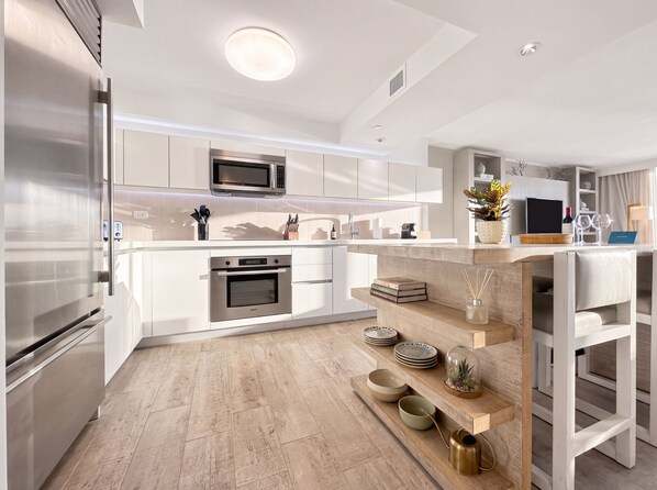 Une cuisine moderne dotée d’appareils électroménagers en acier inoxydable, de meubles blancs et d’un îlot central en bois agrémenté d’objets décoratifs.