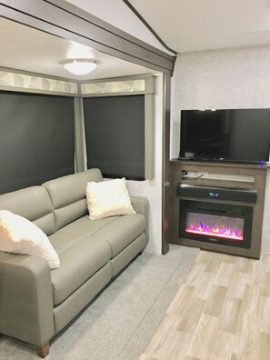 Una sala de estar con sofá, televisión de pantalla plana y chimenea.