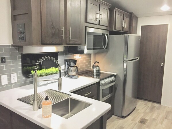 Una cucina moderna con pensili in legno scuro, elettrodomestici in acciaio inossidabile, un forno a microonde integrato e un bollitore in acciaio inossidabile sul piano di lavoro.