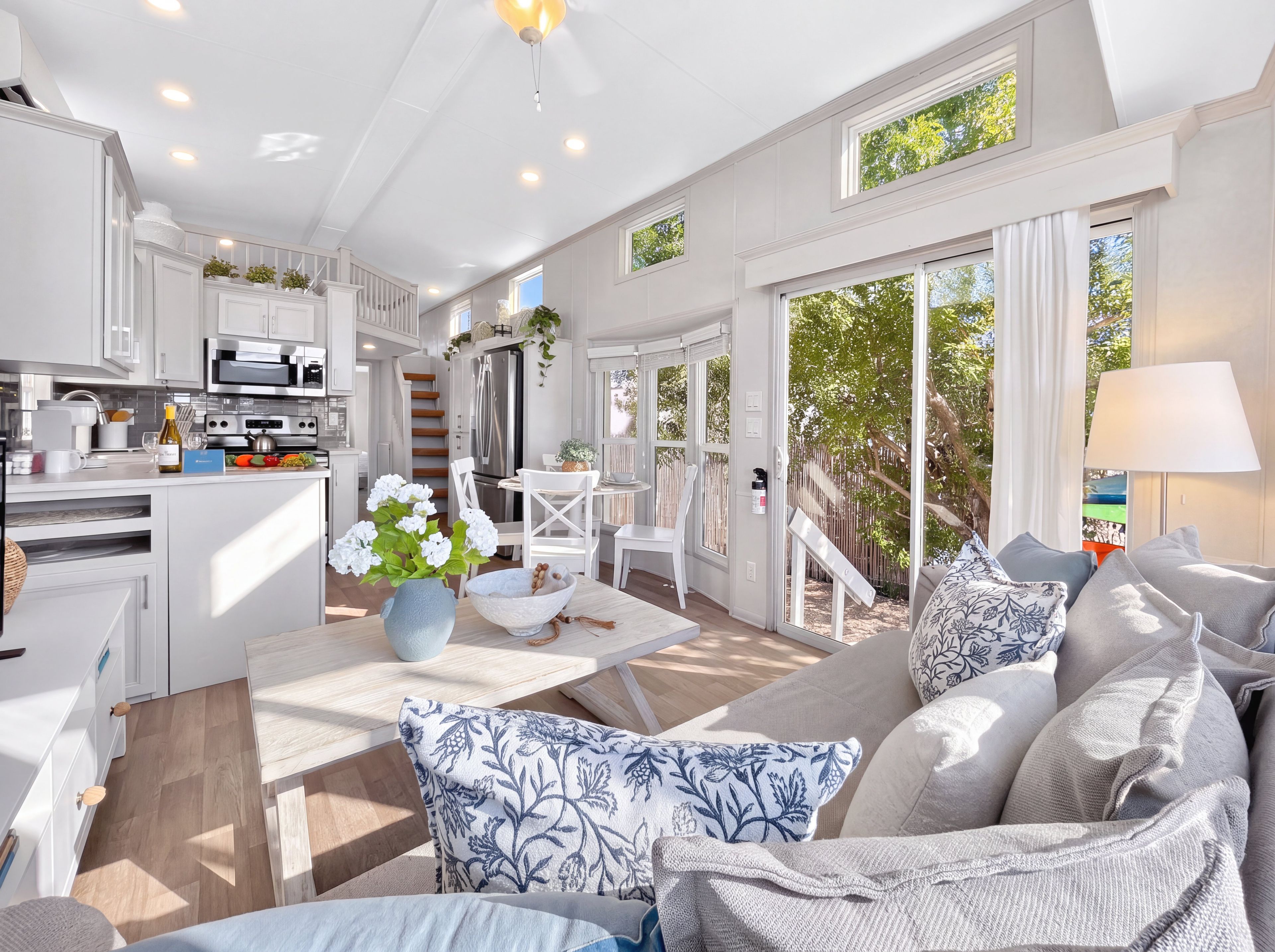 A modern kitchen with white cabinetry, a dining area with a white table and chairs, and a living room with a sofa and decorative pillows.