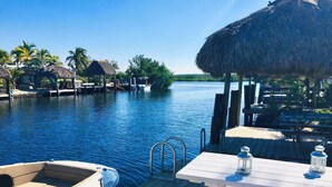 A wooden dock with a boat, a table with a lantern, and thatched-roof structures in the background. - Waterfront Tiny Home w/ Pool, Beach, Dock, Kayaks (Key Largo)