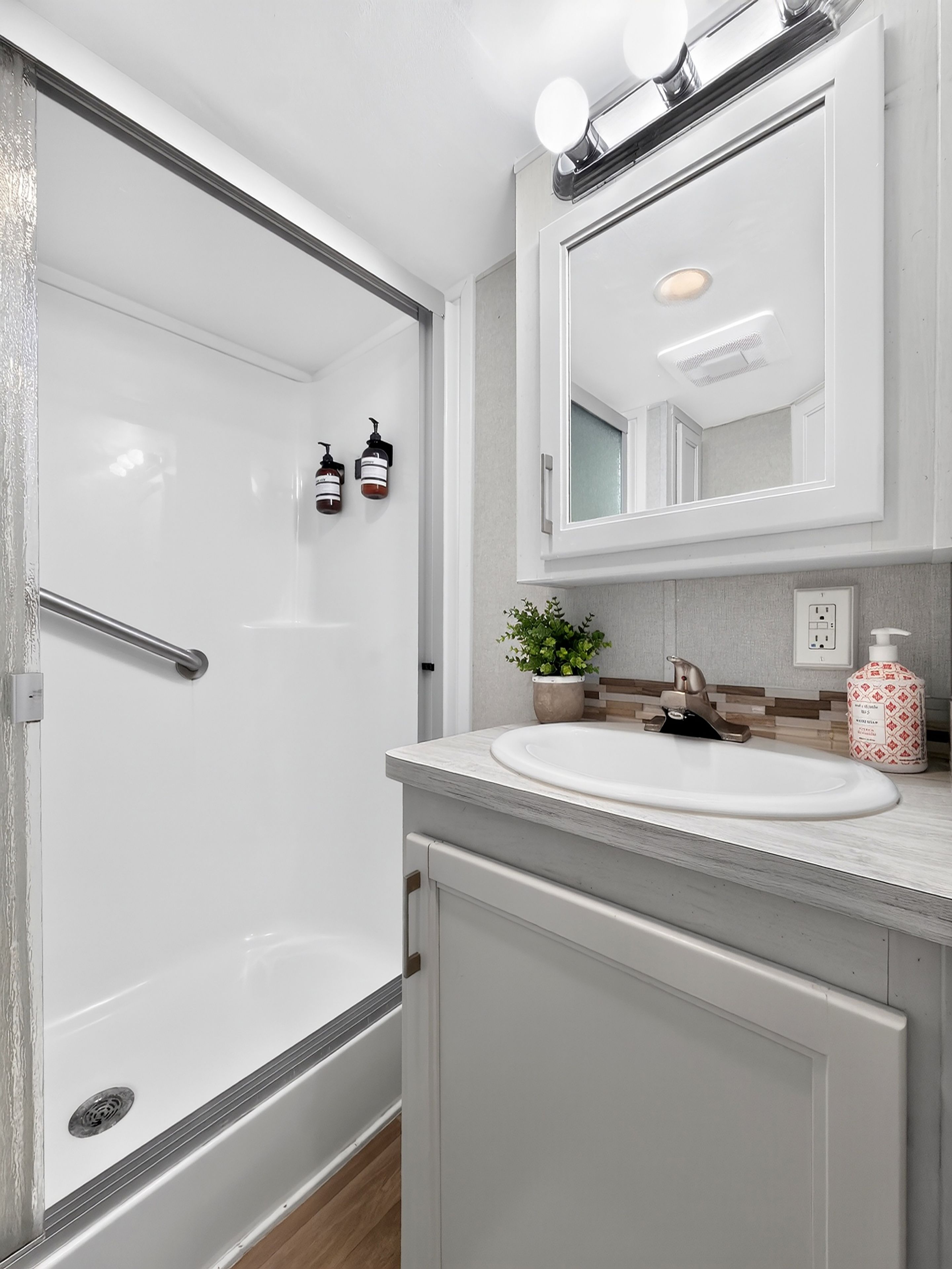 A modern bathroom with a glass shower enclosure, a white sink with a single faucet, and a mirror above the sink.