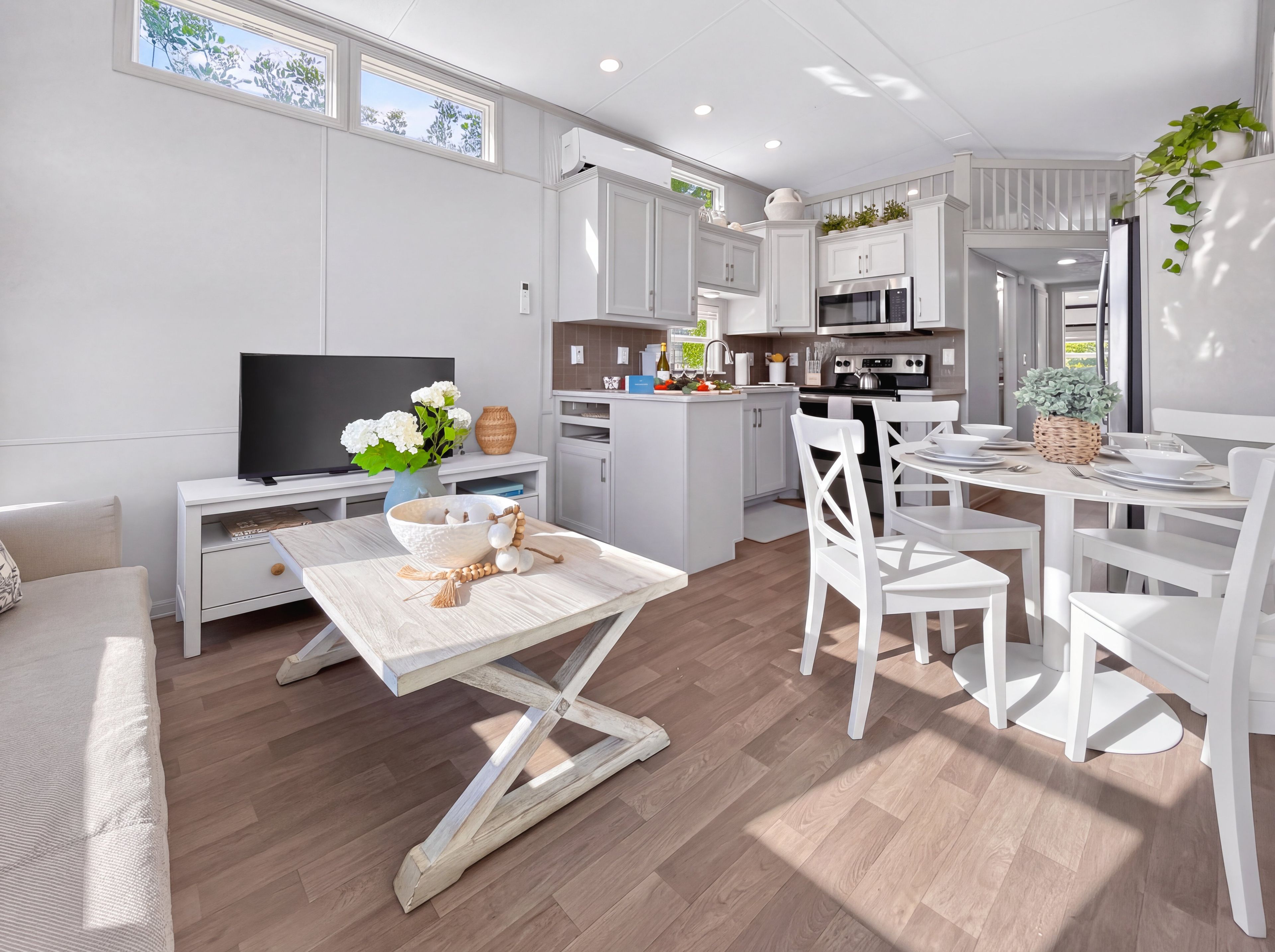 A modern kitchen with white cabinetry, a dining area with white chairs, and a television on a white stand.