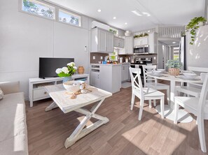 A modern kitchen with white cabinetry, a dining area with white chairs, and a television on a white stand.