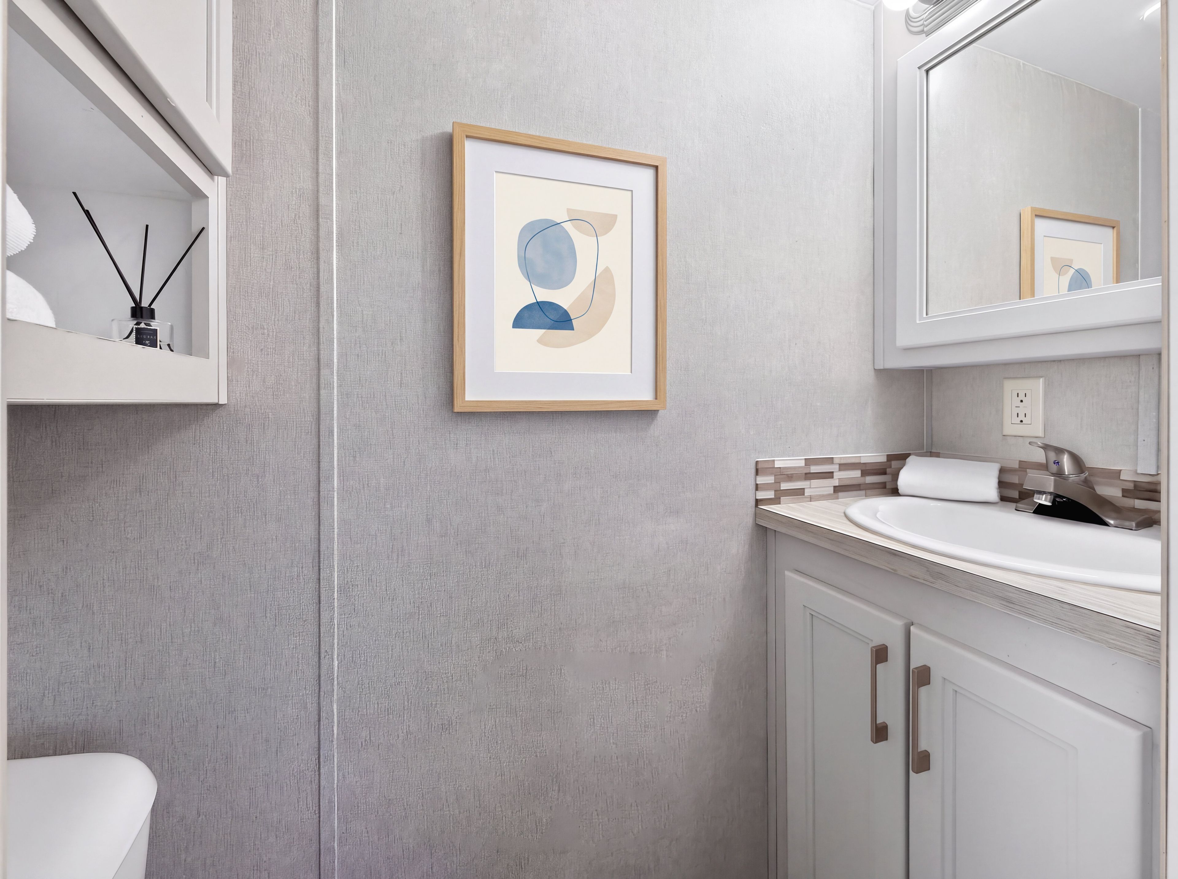 Une salle de bain avec un lavabo blanc, un miroir et une œuvre d’art abstraite encadrée accrochée au mur.