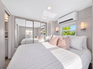 A bedroom with a large bed, a sliding glass door leading to a balcony, and an air conditioning unit on the wall. - Waterfront Tiny Home w/ Pool, Beach, Dock, Kayaks (Key Largo)