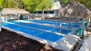 Ein Poolbereich mit blauem Boden, strohgedeckten Gebäuden und einem Zaun.